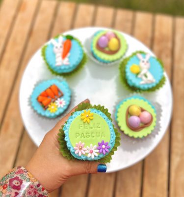 Encantadores cupcakes temáticos de Pascua decorados con conejitos, huevitos y zanahorias en fondant sobre un frosting celeste.