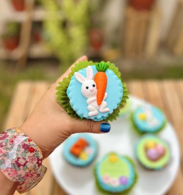 Encantadores cupcakes temáticos de Pascua decorados con conejitos, huevitos y zanahorias en fondant sobre un frosting celeste.