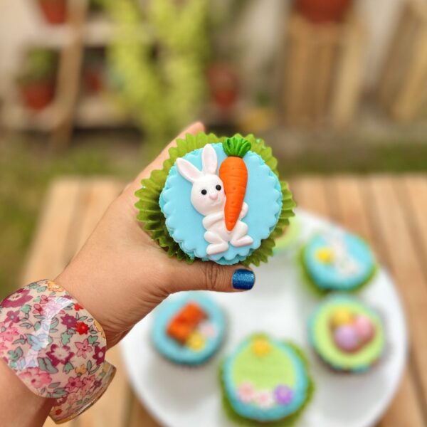 Encantadores cupcakes temáticos de Pascua decorados con conejitos, huevitos y zanahorias en fondant sobre un frosting celeste.
