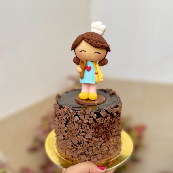 Encantadora mini torta de chocolate decorada con una figura de mamá cocinera y un topper dorado para celebrar el Día de la Madre.