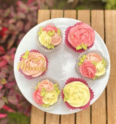 Seis cupcakes decorados con rosetones de buttercream y topper de Mamá con medio corazón.