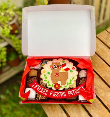 Veinte postres surtidos decorados con fondant con diseño de llama y bandera del Perú, presentados en una caja verde con tramas vintage.