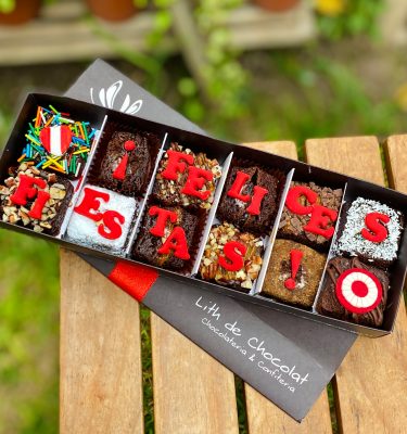 Doce brownies decorados con fondant y detalles de escarapela, presentados en una caja de diseño marrón vintage con lazo de tela.