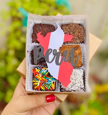 Seis postres decorados con toppings y toppers de la silueta del Perú, empaquetados en una caja ecológica con opción de sticker personalizado.