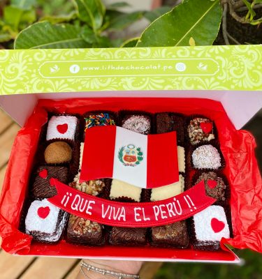 Veinte postres surtidos decorados con arte en oblea de la bandera del Perú, presentados en una caja de diseño marrón vintage con lazo de tela