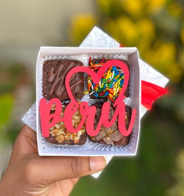 Cuatro mini postres decorados con fondant y toppings, empaquetados en una elegante caja gris con lazo.