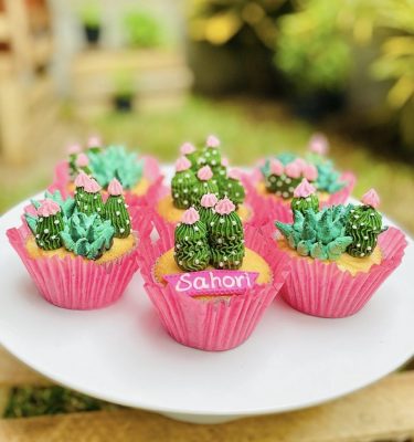 Set de 6 cupcakes de vainilla y chocolate decorados con buttercream verde en forma de cactus y pequeñas flores, empaquetados en una caja blanca con ventana.