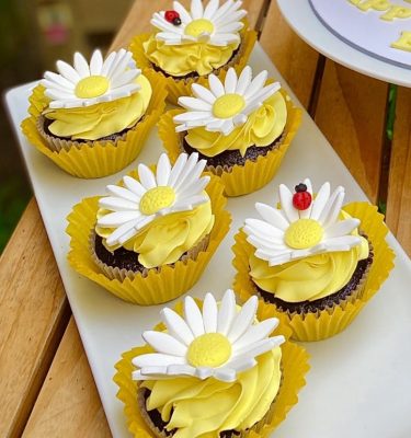 Set de 6 cupcakes de vainilla y chocolate decorados con buttercream amarillo bebé y margaritas con pequeñas mariquitas, empaquetados en una caja blanca con ventana.