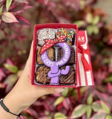 Mini six con 6 brownies y una decoración central del símbolo de la mujer con bandana levantando el brazo y mostrando el músculo, inspirado en la fuerza de la mujer por su día.