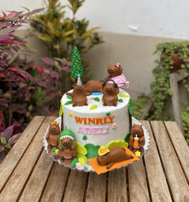 Torta decorada con ocho capibaras, cuatro en la parte superior y cuatro en la parte inferior, cada una con accesorios distintos como tutú, audífonos y sombrero de dinosaurio.