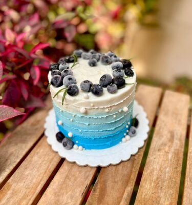 Torta pequeña decorada con buttercream en tonos blanco y celeste, adornada con arándanos frescos, ramitas de romero y perlitas comestibles, ideal para regalar en el Día del Padre.