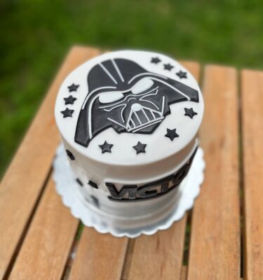 Torta de un piso con acabado en fondant, decorada con el logo de Darth Vader en la parte superior y estrellas alrededor.