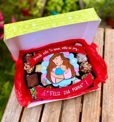 Caja surtida con brownies, trufas y alfajores variados, decorada con topper de fondant de una mamá con su bebé y la frase “Donde está tu amor, está mi paz. Feliz día, mamá”.