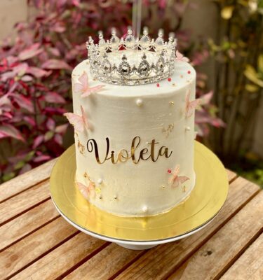 Torta blow cake bañada en buttercream, decorada con corona dorada, mariposas y brillito, con nombre personalizado.