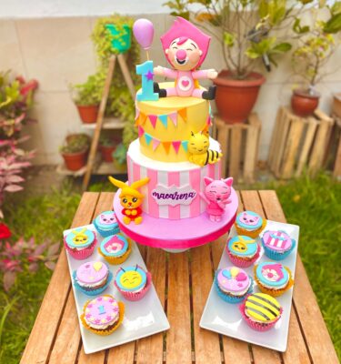 Torta de dos pisos Plim Plim en tonos rosados con personajes del dibujo, incluyendo Plim Plim, la abejita, el gatito y el conejito.