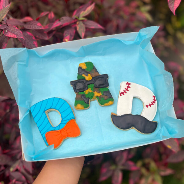 Pack de tres galletas con las letras “DAD”: una “D” decorada con temática de baseball y bigote, la “A” con estilo militar, y la otra “D” con una corbata michi.
