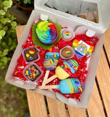 Box sorpresa temática Pride con cupcake, brownies, trufas, alfajor y lacypops decorados con colores de la bandera del orgullo.