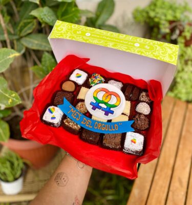 Mix Box con decoraciones en fondant de dos símbolos de mujeres con los colores de la bandera Pride, acompañado de un banner que dice “Mes del Orgullo”.
