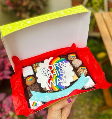 Mix Box con decoración fondant con un círculo blanco, colores de la bandera Pride, la frase “Born This Way” y un banner con fragmento de canción.