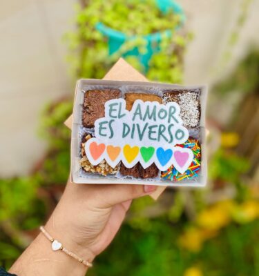 Caja con 6 brownies decorados con un topper de papel de arroz que dice “El amor es diverso” y corazones con los colores de la bandera del Pride.