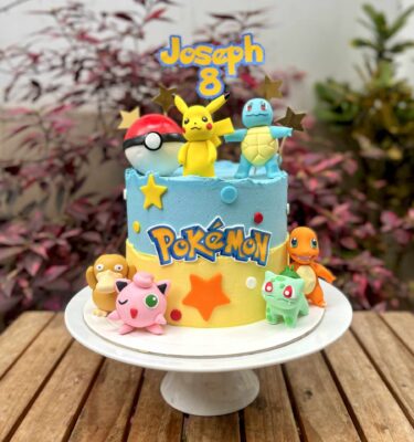 Torta temática de Pokémon decorada con buttercream en tonos celeste y amarillo. Incluye seis figuras de Pokémon y una Pokebola modeladas en fondant.