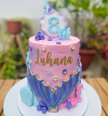 Torta de sirena de un piso, decorada con buttercream y detalles de fondant como conchitas, algas y una ola de sirena en el centro.