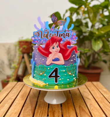 Torta de un piso inspirada en La Sirenita, bañada en buttercream y decorada con toppers de cartulina del personaje y elementos marinos.