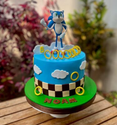 Torta temática de Sonic, cubierta en fondant azul, decorada con Sonic en 3D en la parte superior y aros dorados de fondant alrededor.