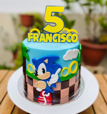 Torta de Sonic en fondant con detalles de palmeras, aros dorados, línea de carrera y figura 2D de Sonic.