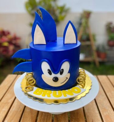 Torta de un piso cubierta en fondant azul que simula el rostro de Sonic, con detalles en fondant para los ojos, orejas y hocico, decorada en la base con aros dorados inspirados en el videojuego.