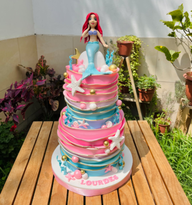 Torta de dos pisos decorada con fondant, Ariel en 3D en la parte superior y elementos marinos como estrellas de mar, conchitas y corales.