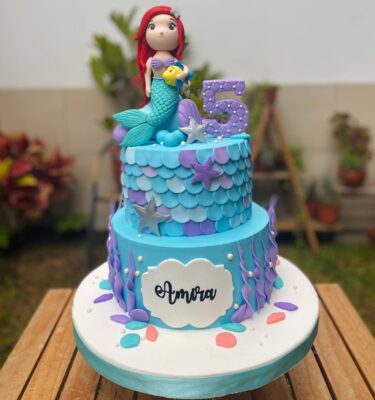 orta de dos pisos inspirada en La Sirenita, con figuras en fondant de Ariel y Flounder, y detalles marinos decorativos.