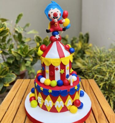Torta de dos pisos con temática de circo, decorada completamente en fondant. En la parte superior está Plim Plim, con colores vivos y detalles inspirados en un show infantil lleno de alegría.