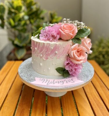 Torta de un piso bañada en buttercream, decorada con flores naturales en tonos delicados.