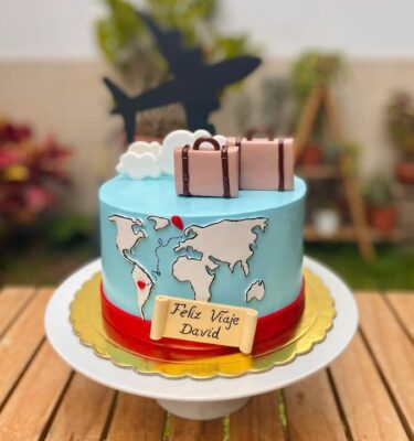Torta viajera decorada con fondant, mapa del mundo, maletas, nubes y topper de avión, ideal para amantes de los viajes.