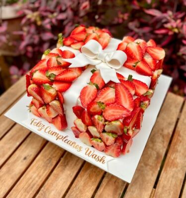 Torta cuadrada decorada con fresas frescas y un elegante moño al centro.