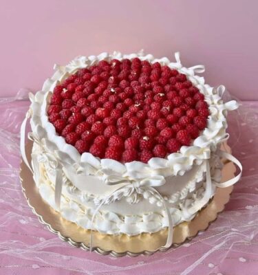 Torta decorada con frambuesas frescas, cintas de tela y bañada en buttercream.