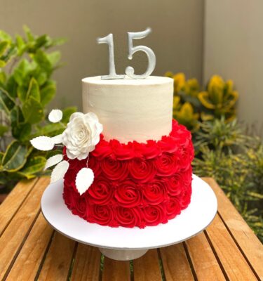 Torta de dos pisos para quinceañero, decorada con rosetones de buttercream en la base, un segundo piso liso y flores naturales en el lateral.