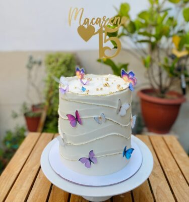 Torta de un piso bañada en buttercream, decorada con mariposas de papel de arroz en los costados y un topper dorado personalizado.