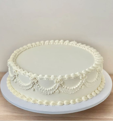 Torta de boda circular bañada en buttercream, decorada con un topper de iniciales en dorado o plateado.