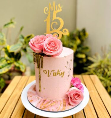 Torta de un piso bañada en buttercream con drip dorado, flores naturales y topper personalizado en dorado.
