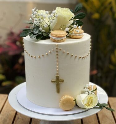 Torta de un piso para Primera Comunión, decorada con macarons franceses, flores naturales, perlas comestibles y una cruz de fondant al centro.