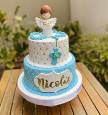 Torta de dos pisos para bautizo, forrada en fondant con textura capitoné, decorada con un niño en 3D de azúcar, rosario en 3D y perlas comestibles que aportan elegancia y simbolismo.