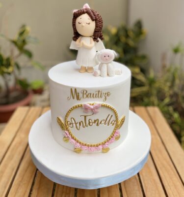 Torta de bautizo en fondant, con niña en 3D de azúcar, ovejita, marco floral y topper dorado.