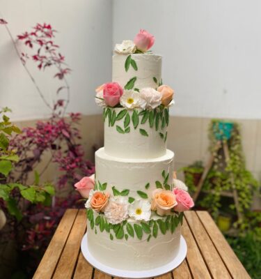 Torta de tres pisos para quinceañero, decorada con hojas de buttercream verde y flores naturales variadas en cada nivel.