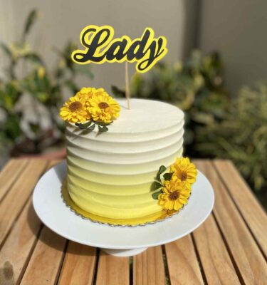 Torta de un piso bañada en buttercream blanco y amarillo, decorada con flores naturales amarillas en la parte superior y los laterales.