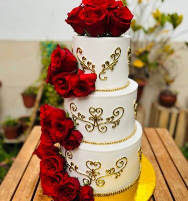 Pastel de quinceañero de tres pisos, decorado con rosas rojas naturales y detalles en fondant dorado, elegante y sofisticado.