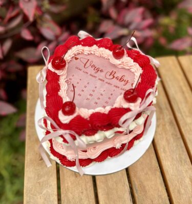Torta Burncake en forma de corazón, decorada en tonos rojo, rosado pastel y blanco, con lazos a los lados, rosetones hechos con diferentes boquillas y cuatro cerezas brillantes en la parte superior.
