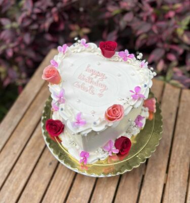Torta en forma de corazón, bañada en buttercream y decorada con flores naturales en tonos suaves.