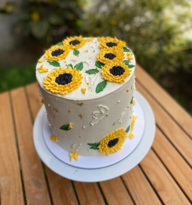 Torta bañada en buttercream, decorada con girasoles de buttercream en la parte superior y en los laterales.